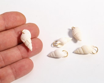 May include: Small, white seashell charms with gold-colored loops for jewelry making. The charms are in various shapes and sizes, with a natural, textured appearance. One charm is held in a person's hand, while the others are scattered on a white surface.