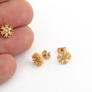 May include: A pair of gold snowflake stud earrings with clear crystal accents.