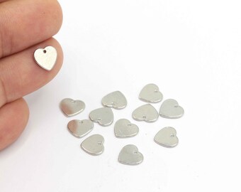 May include: A group of silver heart-shaped charms with a small hole at the top. The charms are scattered on a white surface.