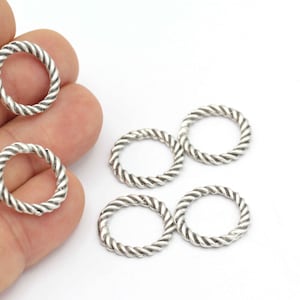 May include: Five silver-toned metal jump rings with a twisted rope design. The rings are approximately 1 inch in diameter.