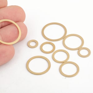 May include: A set of eight gold-colored metal jump rings of varying sizes. The rings are arranged in a cluster on a white surface.