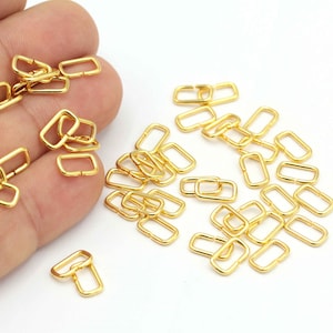 May include: A large quantity of gold-colored metal rectangular jump rings. The rings are small and have a smooth finish.
