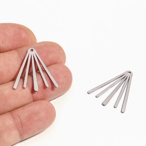 以下が含まれることがあります： 2つの銀色の金属製イヤリングコンポーネント。各コンポーネントは上部に小さな穴があり、5つのまっすぐな平らなバーが扇状に広がっています。1つは手で持ち、もう1つは白い背景にあります。