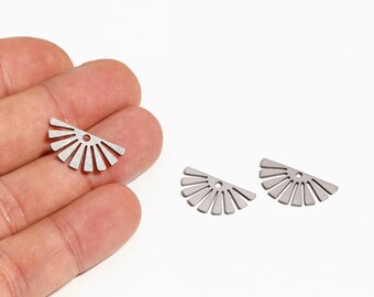 May include: Three silver-colored, fan-shaped metal charms. Each charm has a series of straight lines radiating from a central point, resembling a stylized sun or burst. One charm is held in a hand, while two others are on a white surface.