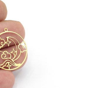 May include: Gold-toned metal charm featuring a crescent moon, stars, and clouds in a circular design.