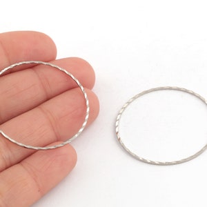 May include: Two silver metal hoops with a textured, diamond-shaped pattern.