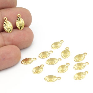 以下が含まれることがあります： 太陽の光線デザインの金色の金属製チャーム12個セット。チャームは楕円形で、上部に小さなループが付いており、ジュエリーやその他のクラフトに取り付けることができます。