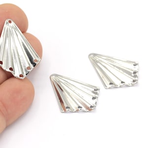 May include: Three silver metal fan-shaped embellishments with holes for attaching to a project. The embellishments have a textured, ribbed surface.