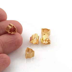 May include: Five gold-colored metal flower-shaped charms. The charms are small and have a delicate design.