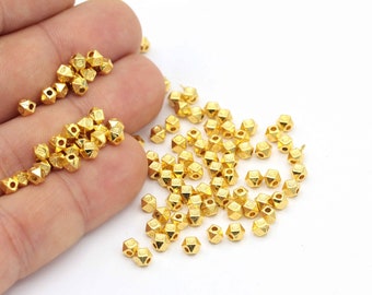 May include: A pile of gold-colored metal beads with a faceted, pyramid-like shape. The beads have a hole in the center for stringing.