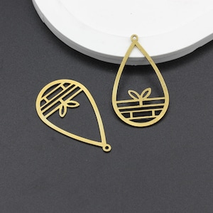 May include: Two gold metal pendant charms in the shape of a teardrop. Both charms have a geometric design with a small plant inside.