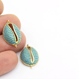Könnte beinhalten: Zwei muschelförmige Anhänger in Goldton mit türkisblauen Mikropavé-Steinen. Jeder Anhänger hat eine Öse zum Anbringen an einer Halskette oder einem Armband.