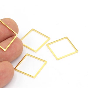 May include: A collection of gold-colored square jewelry findings. The findings have a square frame with a white interior. One is held in a hand, and the others are scattered on a white surface. These findings are ideal for DIY jewelry making.