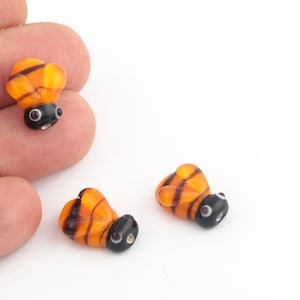 May include: Three small glass bee beads with black and yellow stripes and black eyes. The beads are about 1 inch long.