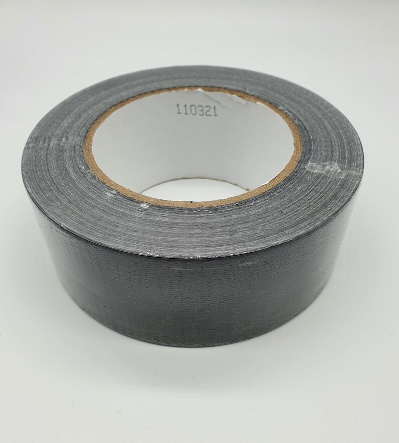 K&ouml;nnte beinhalten: Eine Rolle graues Panzerband mit einem wei&szlig;en Innenkern. Das Klebeband hat eine einfarbige graue Farbe und eine strukturierte Oberfl&auml;che. Die Nummer "110321" ist auf dem Innenkern aufgedruckt.