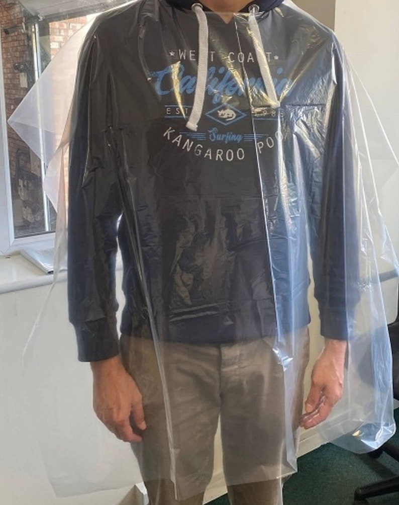 May include: A transparent plastic poncho worn over a navy blue hooded sweatshirt with the text "West Coast California Surfing Kangaroo Point". The person is also wearing khaki shorts.