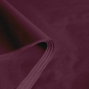 May include: A stack of deep burgundy tissue paper, with a curved edge revealing the layered sheets. The paper has a smooth, matte finish and a rich, saturated color, ideal for gift wrapping or crafting.