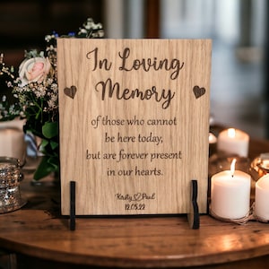 May include: A wooden sign with the text "In Loving Memory" and a message about those who cannot be here today, but are forever present in our hearts. The sign is personalised with the names "Kersty & Paul" and the date "12.05.22".