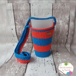 Könnte beinhalten: Ein gehäkelter Becherhalter mit blau-orangem Streifenmuster. Der Halter hat einen langen Trageriemen. Der Text "HakeLstreet Fleur de Lis by Fem Ulla" ist im Bild sichtbar.