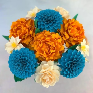 May include: A vibrant bouquet of paper flowers in shades of orange, teal, and cream. The arrangement features large, layered blooms resembling dahlias and roses, with green leaves. A visually striking, handcrafted floral arrangement.