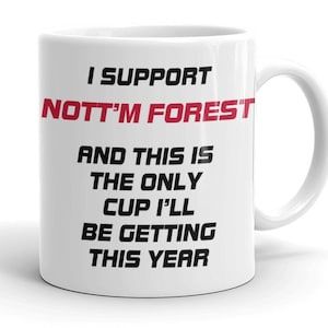 May include: White ceramic mug with the text "I SUPPORT NOTT'M FOREST" in black and red. The mug also says "AND THIS IS THE ONLY CUP I'LL BE GETTING THIS YEAR". The mug has a curved handle.