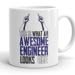 May include: White ceramic mug with a black and blue graphic that reads "THIS IS WHAT AN AWESOME ENGINEER LOOKS LIKE." The design includes two hands pointing upwards. The mug has a curved handle.