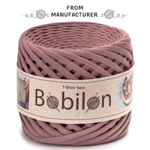 May include: A roll of mauve T-shirt yarn labeled "Bobilon." The yarn is tightly wound, showing a ribbed texture. The label also reads "T-Shirt Yarn" and "From Manufacturer."