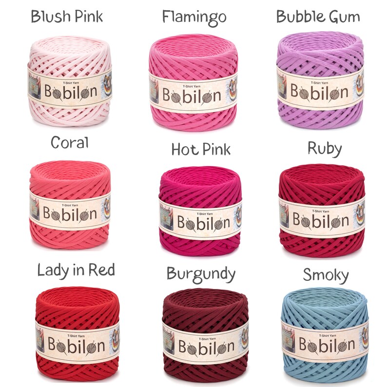 May include: Nine spools of T-shirt yarn in various colors, including blush pink, flamingo, and bubble gum. Each spool has a label that reads "Babilon". The colors range from light pink to deep red and smoky blue.
