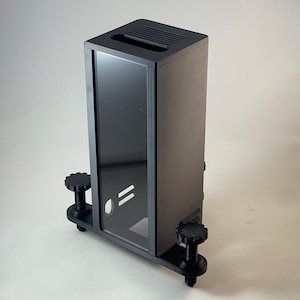 Puede incluir: Un dispositivo electrónico rectangular negro con un panel frontal de vidrio y una parte superior ranurada. El dispositivo está montado sobre una base negra con perillas ajustables. El diseño es moderno y minimalista.