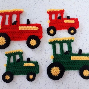 May include: Four handmade crochet tractor appliqués in red and green, with yellow and black accents. The tractors have black wheels with yellow centres. The red tractors have yellow roofs, and the green tractor has a yellow roof. These are likely for crafting or decorating.