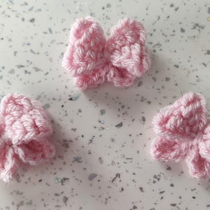 May include: Three pink crocheted bows. The bows are small and delicate, and they would be perfect for adding a touch of whimsy to a craft project.