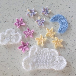 May include: A set of crocheted stars and clouds in various colours, including white, pink, yellow, and blue. The set includes two clouds, a crescent moon, and several stars.