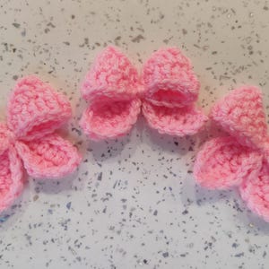 May include: Three pink crocheted bows. The bows are made with a soft, fluffy yarn and have a delicate, feminine look.