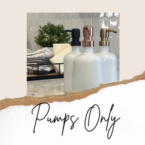 Könnte beinhalten: Drei weiße Keramik-Seifenspender mit verschiedenen farbigen Aufsätzen. Die Spender stehen auf einer weißen Arbeitsplatte mit einem schwarzen Metalltablett und Handtüchern dahinter. Der Text "Pumps Only" ist in schwarzer Kursivschrift auf braunem Papierhintergrund geschrieben.