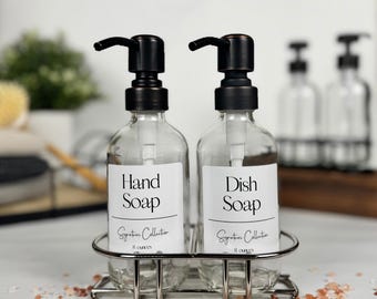 May include: Two clear glass soap dispensers with black pumps, labelled "Hand Soap" and "Dish Soap." The bottles are in a silver metal caddy. Each bottle holds 237 ml. The "Signature Collection" is printed on the label.