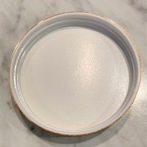May include: White round lid with a gold rim.