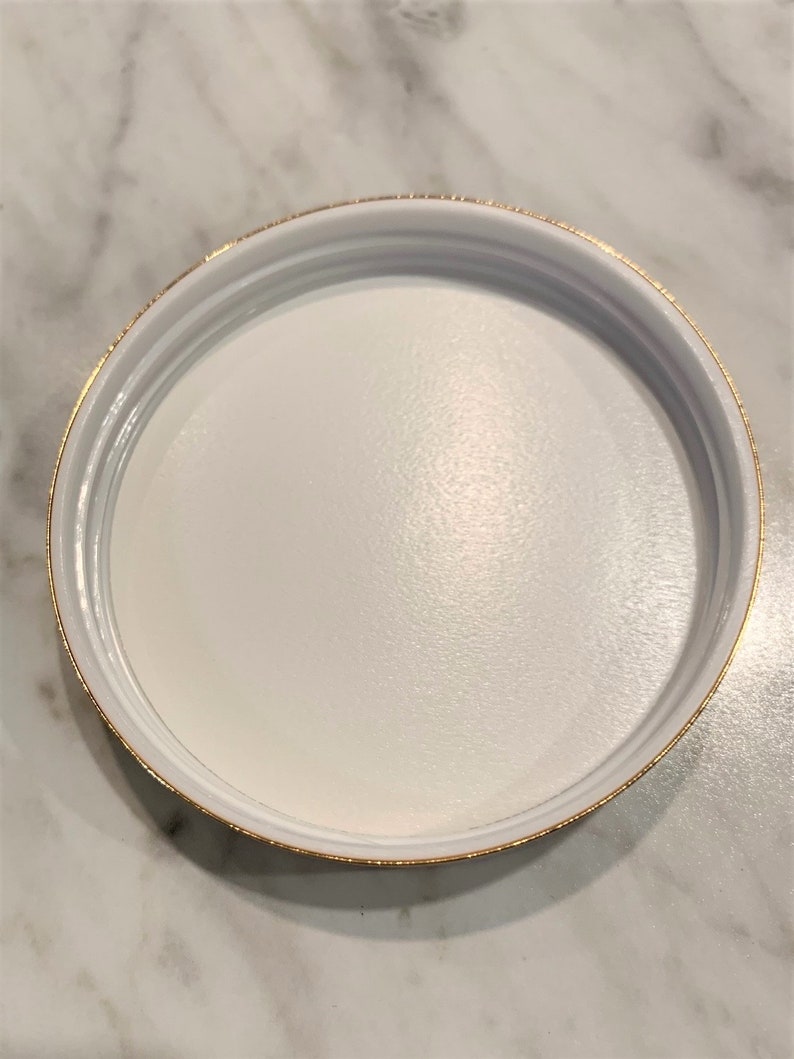 May include: White round lid with a gold rim.