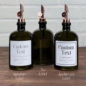 Pu&ograve; includere: Tre bottiglie di vetro ambrato con pompe in rame ed etichette. Le etichette sono bianche con testo nero. Le etichette riportano "Testo personalizzato" e includono i nomi "Signature Collection", "Apothecary Collection" e "Senza etichetta".