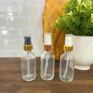 May include: Three glass bottles with gold tops and clear pumps. The bottles are empty and sitting on a wooden surface.