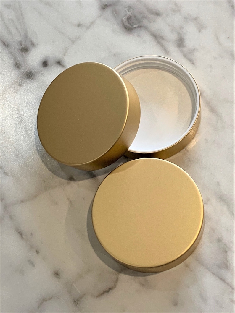 May include: Three gold-colored metal lids for jars or containers. The lids are round and have a smooth surface.