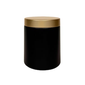 May include: A black cylindrical jar with a gold lid. The jar is made of a smooth, matte material.