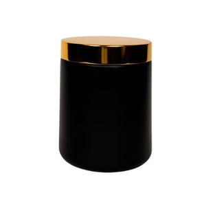 Op de afbeelding: Zwarte keramische pot met een gouden deksel. De pot is cilindrisch en heeft een glad oppervlak.