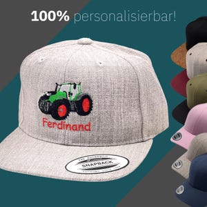 Könnte beinhalten: Hellgraue Snapback-Kappe mit einem gestickten grün-schwarzen Traktormotiv und dem Namen "Ferdinand" in Rot. Der Text "100% personalisierbar!" steht oben. Im Hintergrund sind mehrere weitere Kappen in verschiedenen Farben zu sehen.