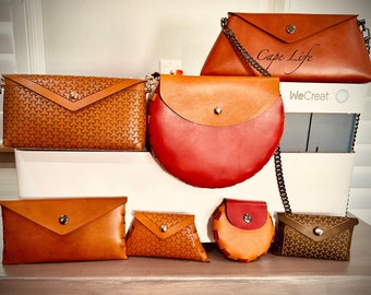 May include: Assortment of six leather purses and wallets in various shapes and sizes. The purses are brown, red, and orange with a variety of textures and patterns. The purses are arranged on a white surface with a box labeled "WeCreat".