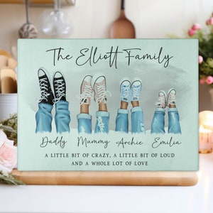 May include: A rectangular, pale green family-themed decorative sign. The sign features illustrations of legs in jeans and trainers, with the text "The Elliott Family" and names below. The bottom text reads "A LITTLE BIT OF CRAZY, A LITTLE BIT OF LOUD AND A WHOLE LOT OF LOVE."