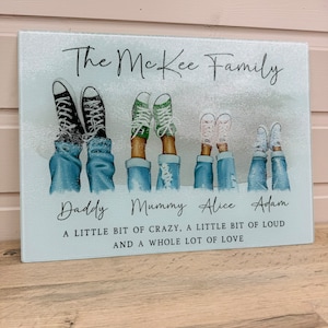 May include: A rectangular glass chopping board with a family design. It shows illustrations of feet in jeans and trainers, with the text "The McKee Family." Additional text reads "A little bit of crazy, a little bit of loud and a whole lot of love."