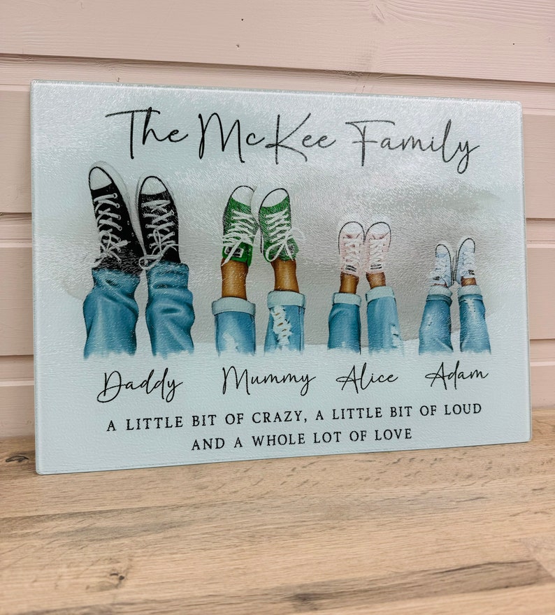 May include: A rectangular glass chopping board with a family design. It shows illustrations of feet in jeans and trainers, with the text "The McKee Family." Additional text reads "A little bit of crazy, a little bit of loud and a whole lot of love."