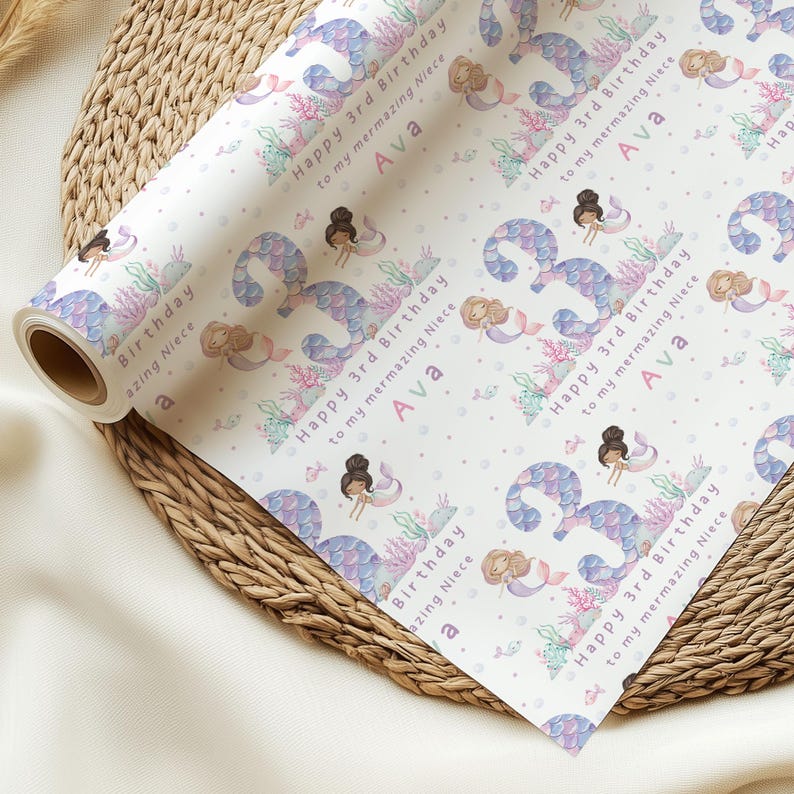 May include: White wrapping paper with a repeating pattern of purple mermaids, seashells, and coral. The text "Happy 3rd Birthday to my mermazing Niece Ava" is repeated throughout the pattern.