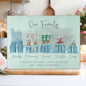 May include: A rectangular, pale green family-themed decorative sign. The sign features illustrations of legs and feet wearing trainers, with the words "Our Family" at the top. Below the illustrations are the names "Daddy, Mummy, Lucas, Charlie, Lucy". The bottom of the sign reads "A LITTLE BIT OF CRAZY, A LITTLE BIT OF LOUD AND A WHOLE LOT OF LOVE".