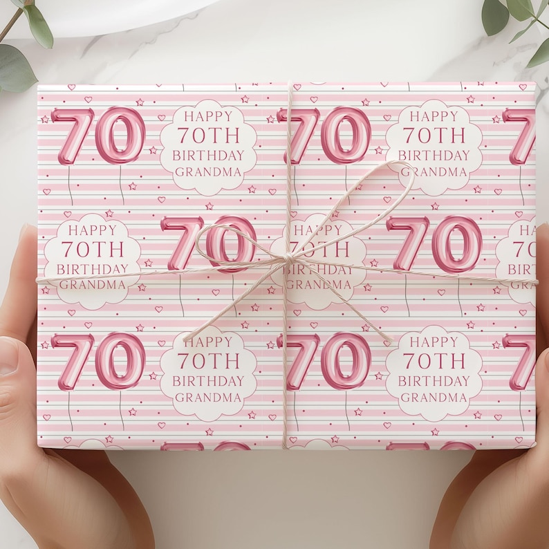 May include: Pink wrapping paper with a repeating pattern of the number 70 in a balloon style, the text "Happy 70th Birthday Grandma", hearts, and stars. The wrapped gift is tied with twine.